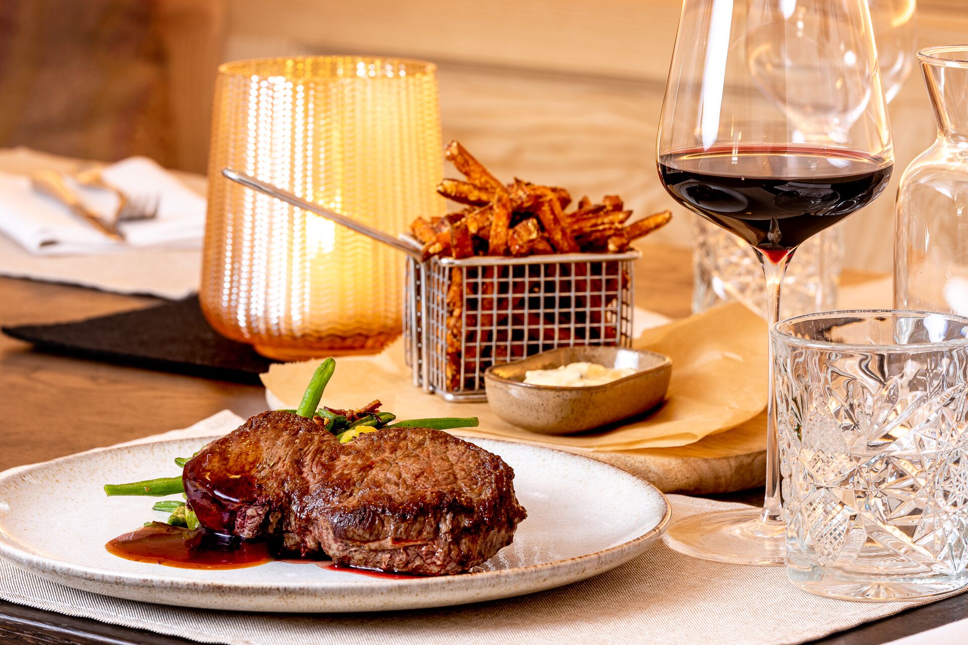 A plate of steak with fries, a glass of red wine, and a candle on a table.