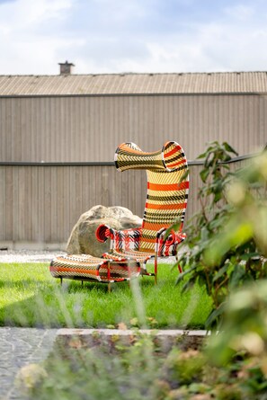 Situated in a lush outdoor setting, this chair offers a serene atmosphere with a well-maintained lawn and a large rock nearby.