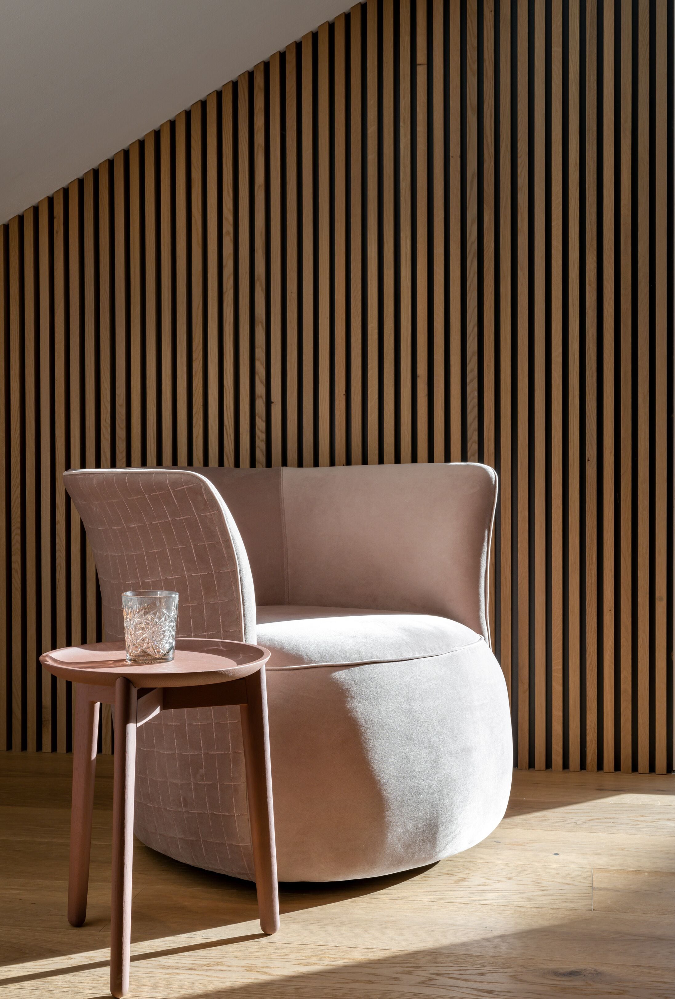 Een modern interieur met een gebogen bank, een klein rond tafeltje en een glas water.