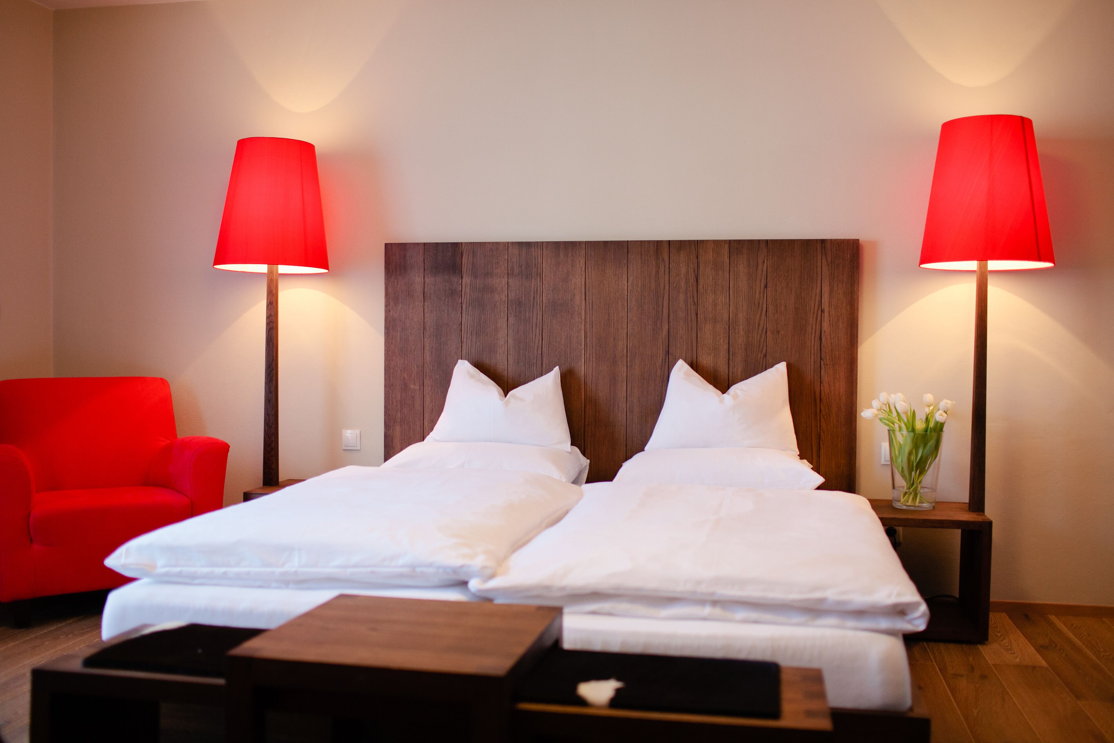 Een hotelkamer met een houten hoofdeinde, twee enkele bedden, een rode stoel en twee bedlampjes.