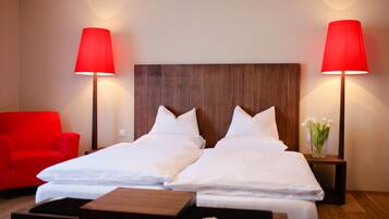 Een hotelkamer met een houten hoofdeinde, twee enkele bedden, een rode stoel en twee bedlampjes.