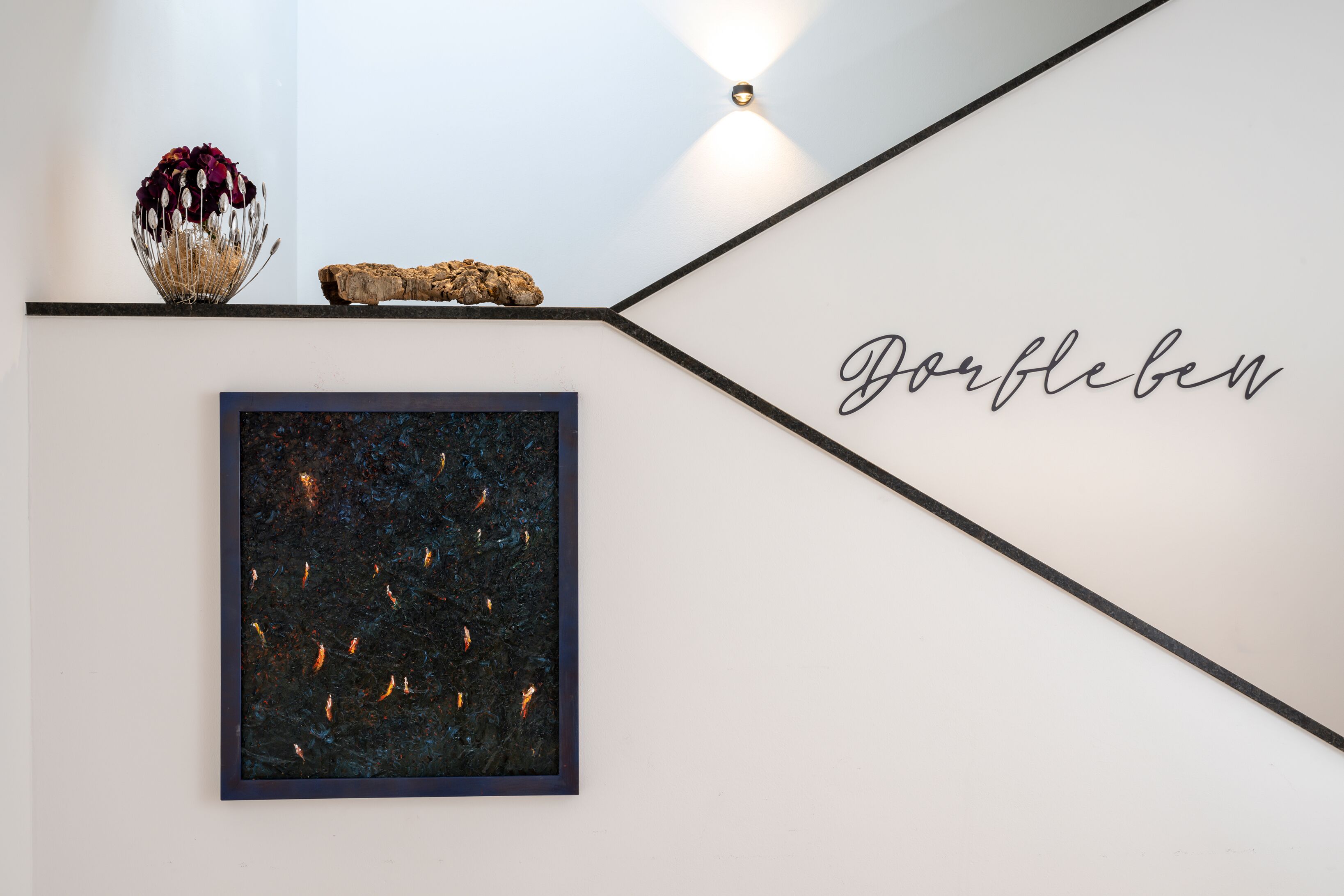 A wall with a framed abstract painting, a decorative vase, and a piece of driftwood. The word "Dorleben" is written on the wall.