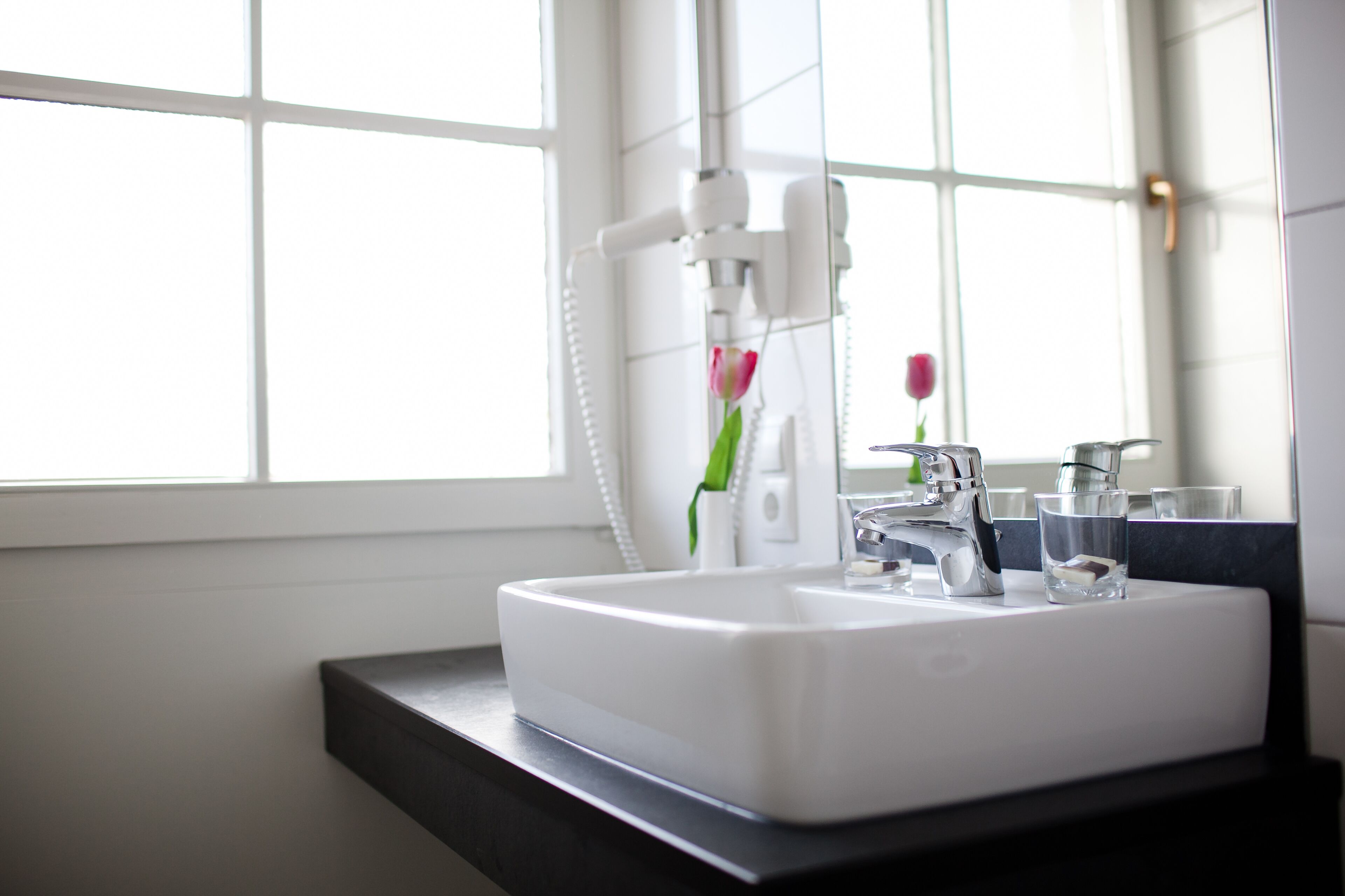 A modern bathroom with a white sink, a mirror, and a window.