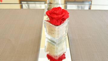 A dining table with a clear glass centerpiece containing a red rose and a decorative item.