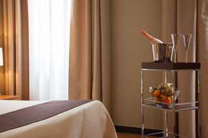 Hotellihuone, jossa on sänky, minibaari, jossa on pullo samppanjaa, kaksi lasia ja kulho täynnä hedelmiä.