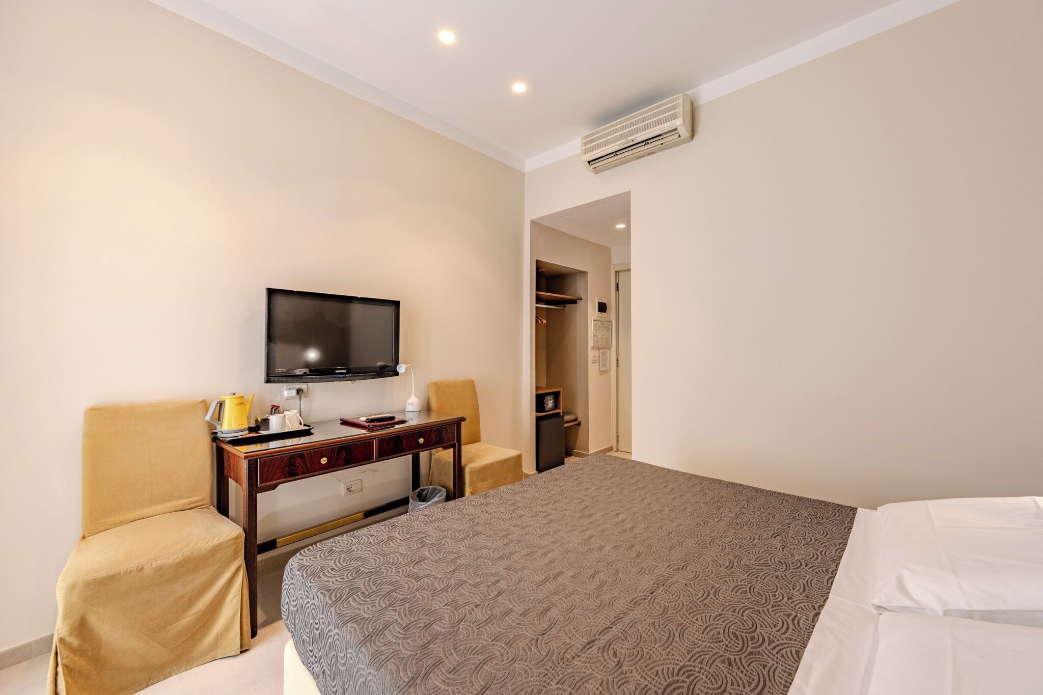 A hotel room with a bed, a desk with a chair, a television, and a wardrobe.