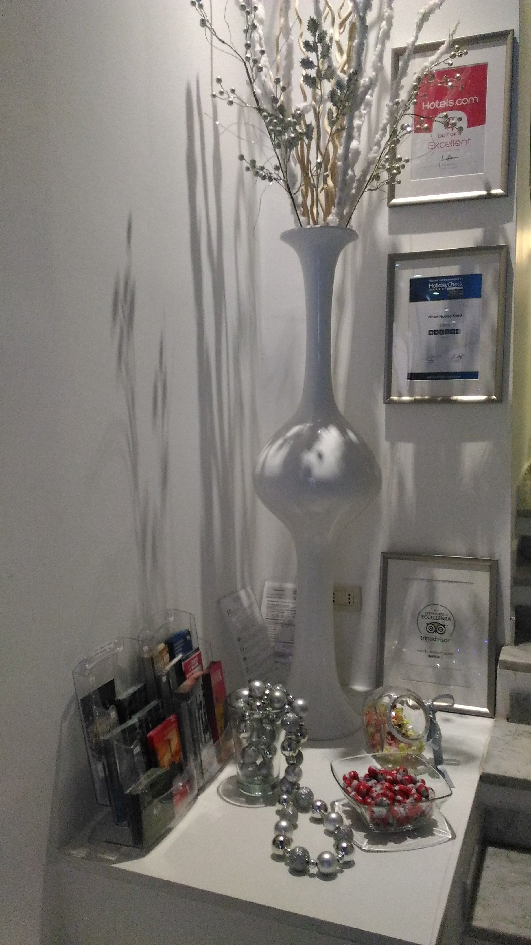 Een receptiebalie met een vaas gedroogde takken, ingelijste onderscheidingen en een glazen display met diverse objecten.
