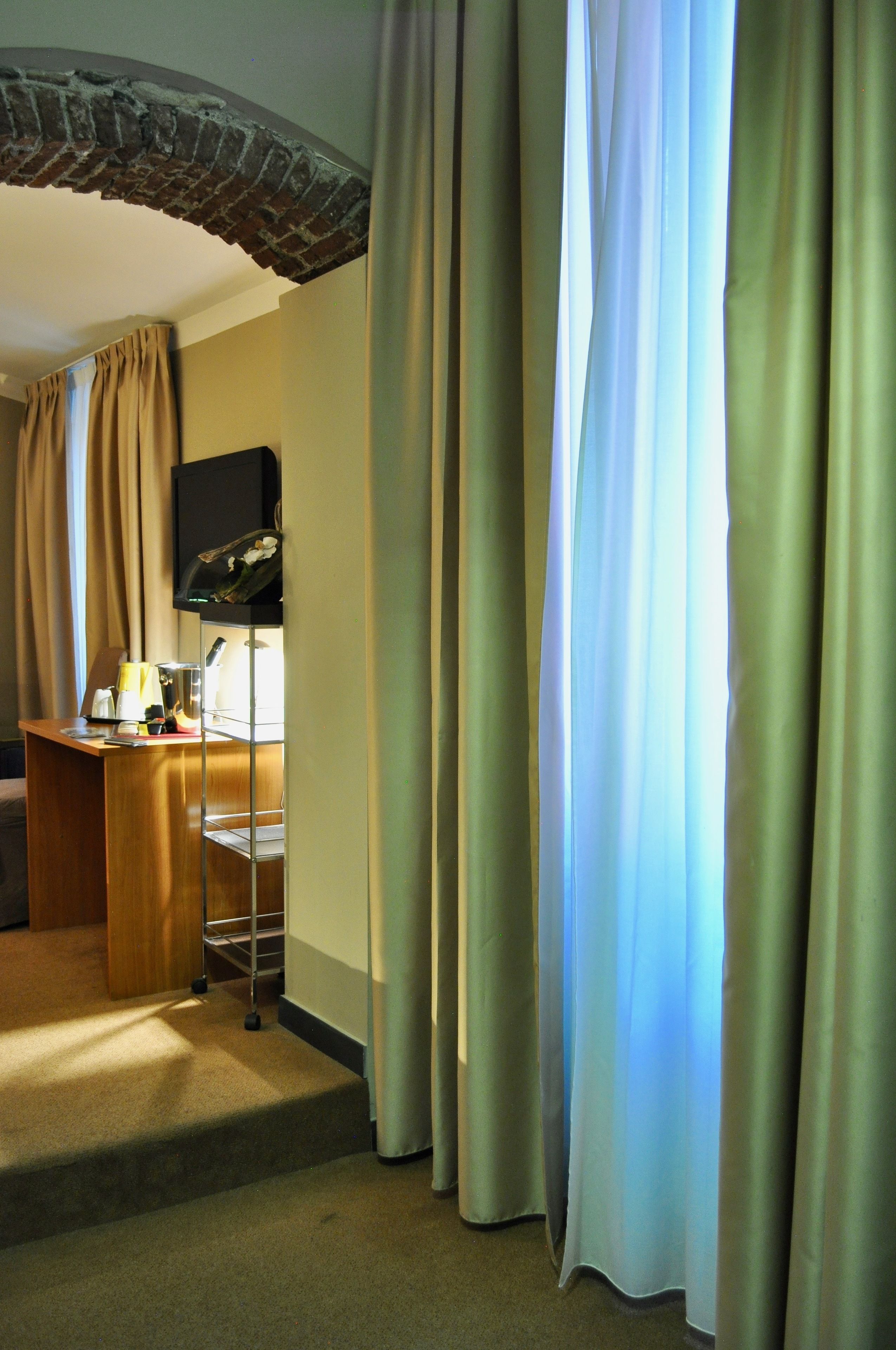 Habitación de hotel con un escritorio de madera, televisión y ventana con cortinas.