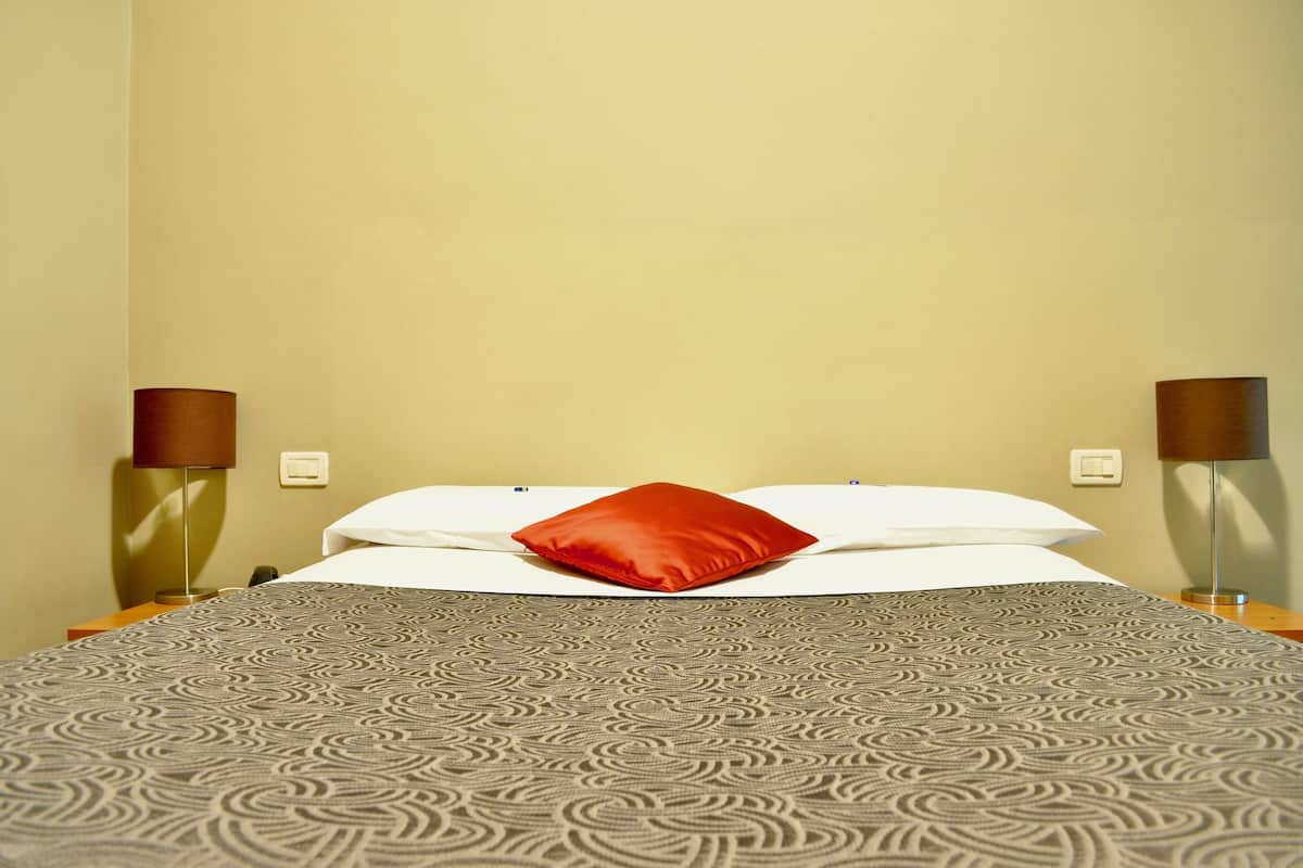 Een hotelkamer met een bed met een patroongordijn, een rood kussen en twee bedlampen.