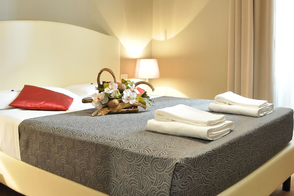 Een hotelkamer met een bed, nachtkastje, lamp en raam met gordijnen.