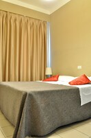 A hotel room with a bed, beige curtains, a lamp, and patterned bedding.