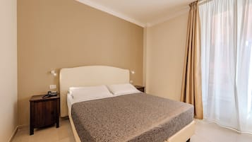 Ein ordentlich eingerichtetes Schlafzimmer mit einem großen Bett, einem Nachttisch mit Telefon und einem Fenster mit transparenten Vorhängen.