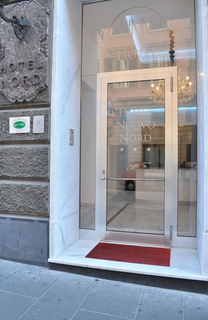 A hotel entrance with a glass door, a red carpet, and a stone wall with a plaque. - Hotel Nuovo Nord (Genoa)