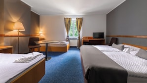Hotellihuone, jossa on kaksi sänkyä, työpöytä, tuoli, televisio ja ikkuna, jossa on verhot.