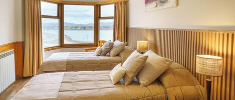 A hotel room with two beds, a view of the sea, a lamp, and a telephone on the nightstand.
