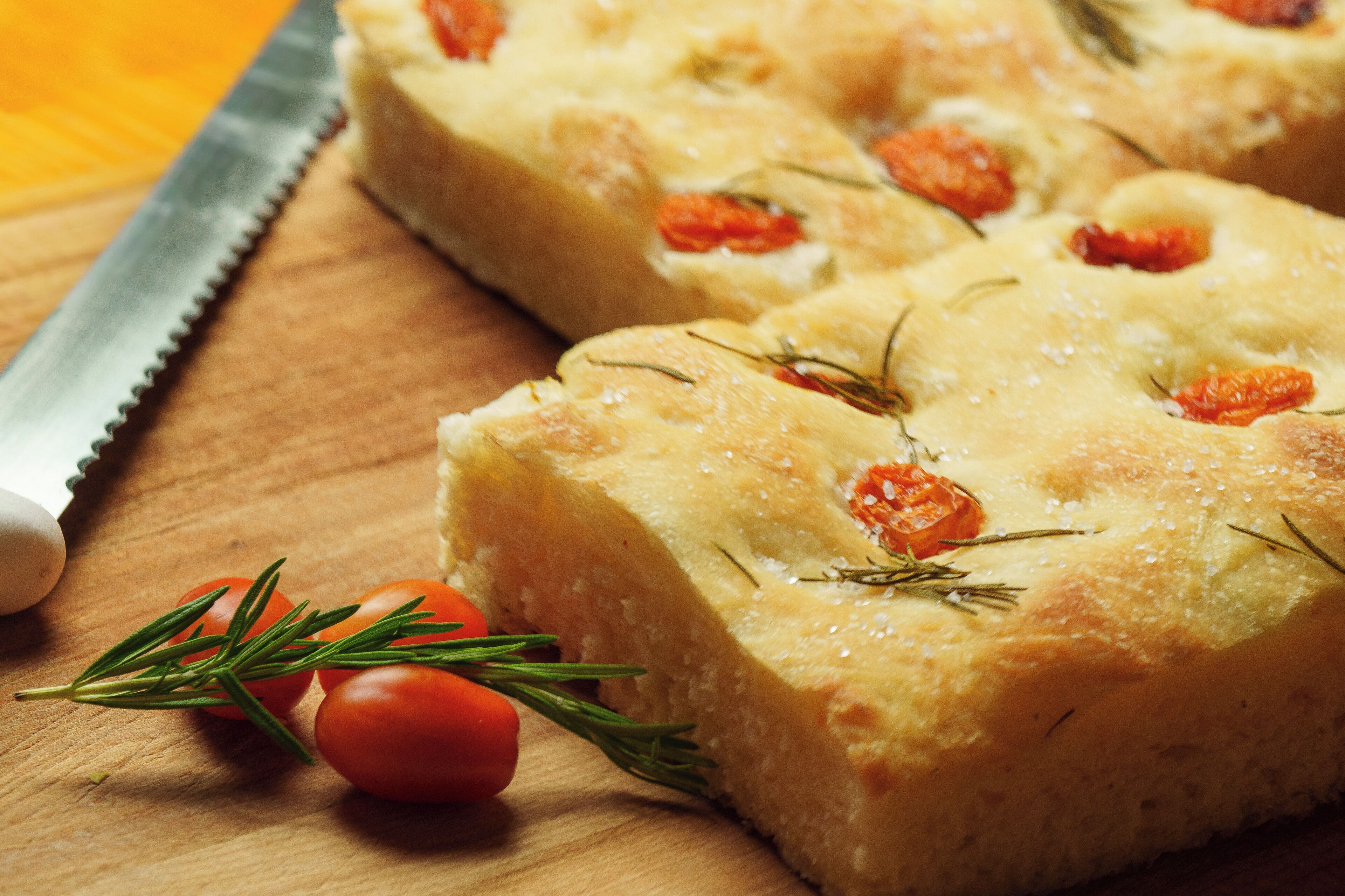 Un trozo de comida rectangular con tomate y romero sobre una superficie de madera.