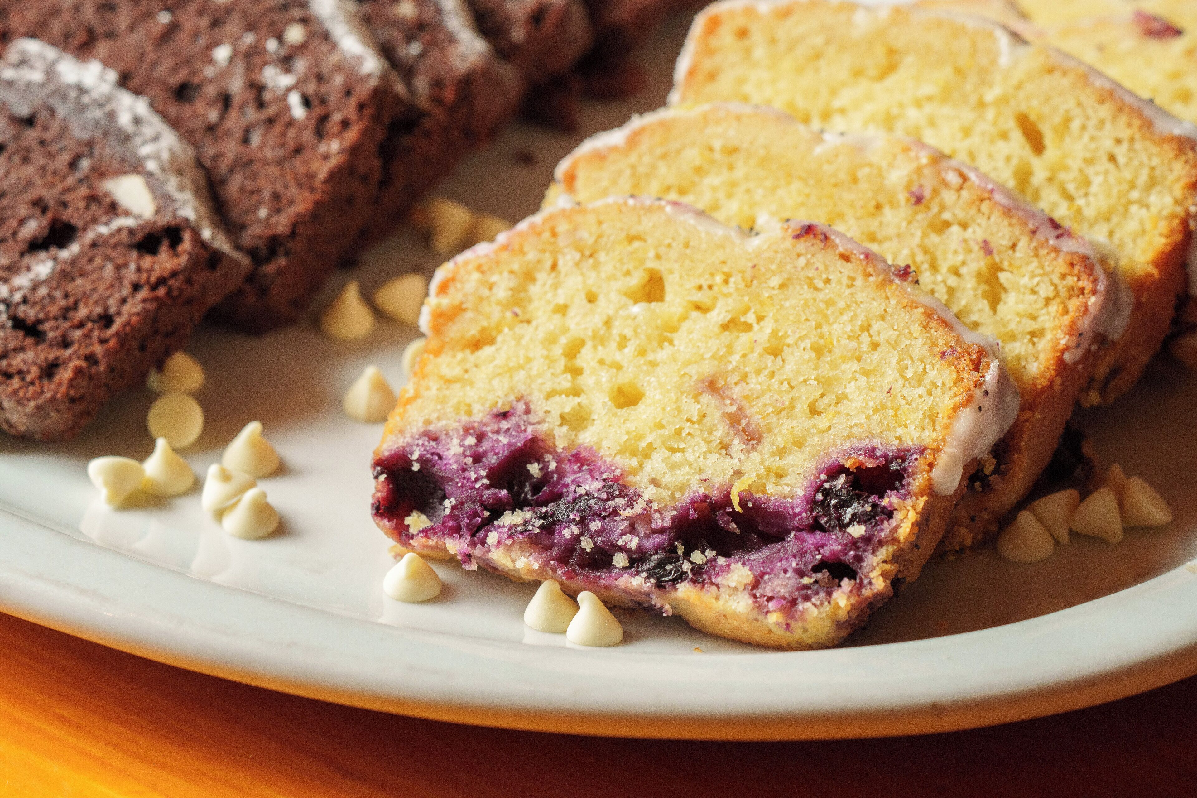 Una fetta di torta ai mirtilli con ripieno cremoso e crosta friabile, insieme a una fetta di torta al cioccolato.