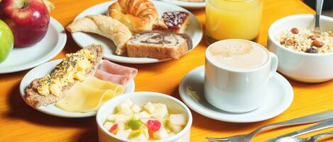 Desayuno con diversos alimentos y utensilios sobre una mesa de madera.