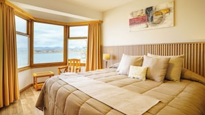 A bedroom with a large bed, a view of the sea, and a wooden headboard. - Los Naranjos (Ushuaia)