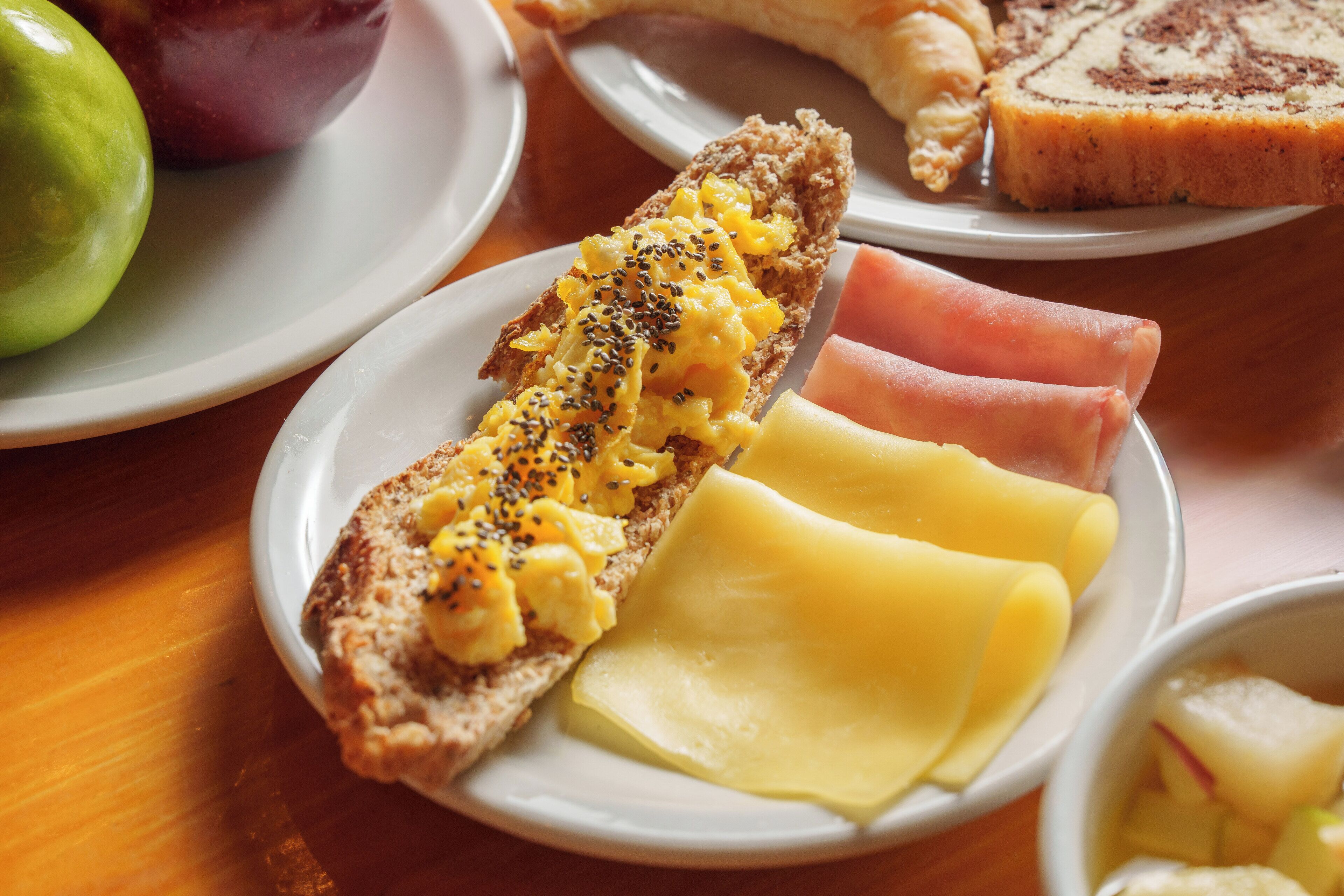 A breakfast plate with scrambled eggs, cheese, ham, and a croissant.