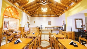 A spacious dining area with wooden tables and chairs, a high wooden ceiling, and a kitchen in the background. - Los Naranjos (Ushuaia)