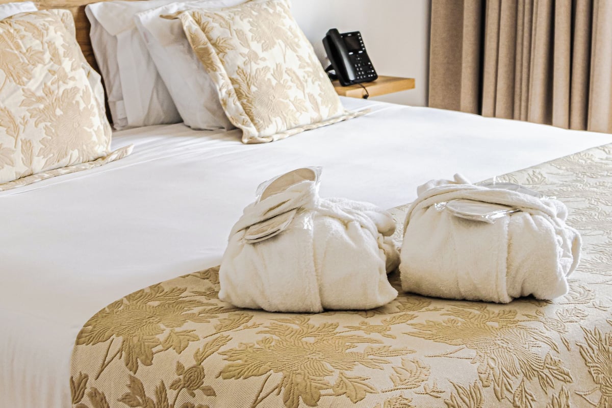 Habitación de hotel con cama, almohadas, mesita de noche con teléfono y pared con listones de madera.