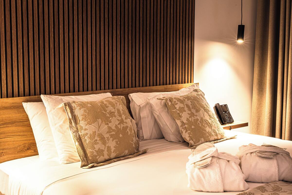 Habitación de hotel con cabecera de madera, teléfono junto a la cama y una cama bien hecha con almohadas estampadas con motivos florales.