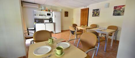 A dining area with a table set for two, chairs, a microwave, and a refrigerator in the background.