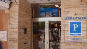 L’entrée d’un hôtel appelé SERRAMAR, avec une enseigne indiquant qu’il s’agit d’une pension et un espace de stationnement.