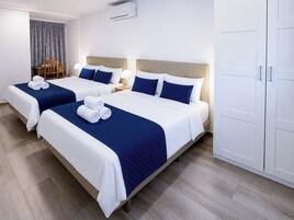 A hotel room with two beds, a wardrobe, and a dining area with a chair and table.