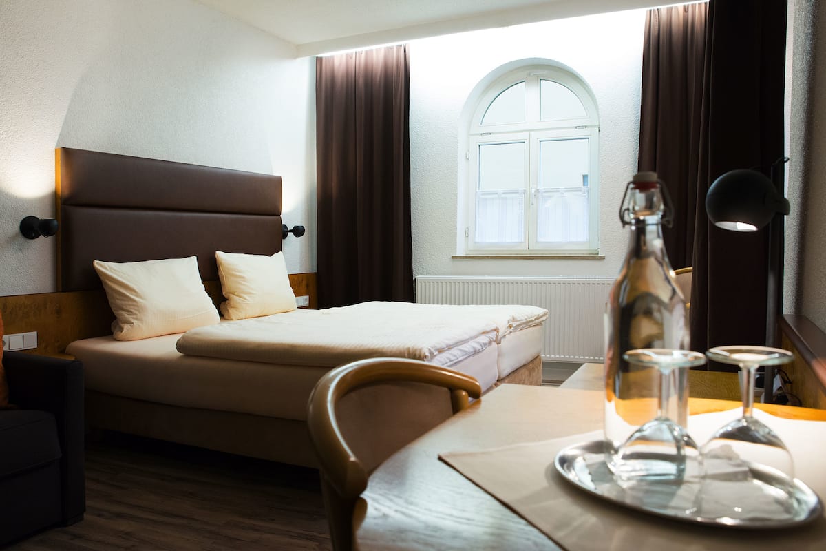 A hotel room with a bed, bedside table, lamp, and a window with curtains.