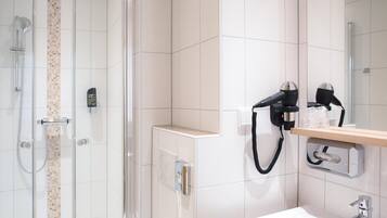 A modern bathroom with a glass shower enclosure, a white sink, and a hairdryer mounted on the wall.
