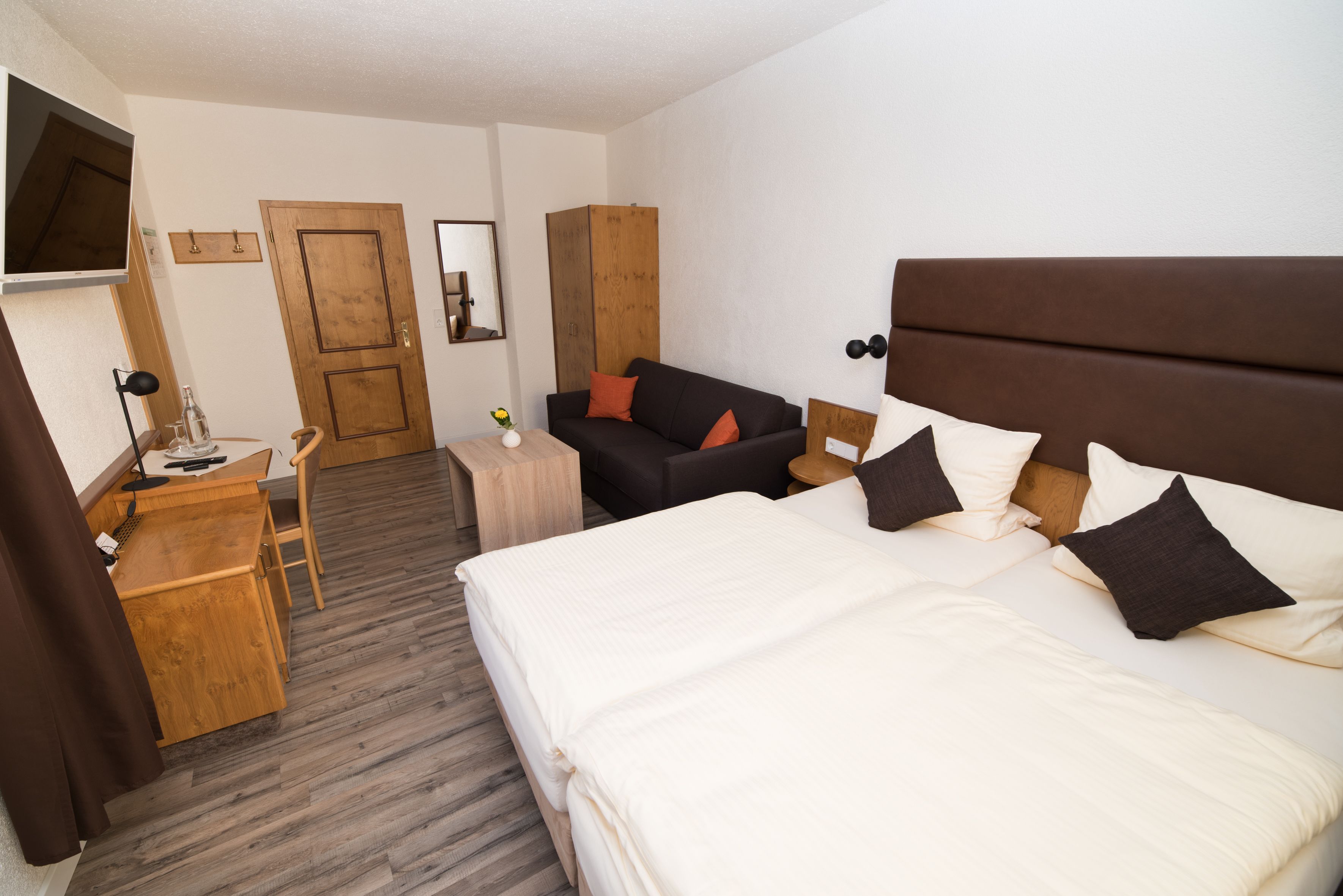 Ein Hotelzimmer mit Bett, Schreibtisch, Stuhl, Kleiderschrank und Fernseher.