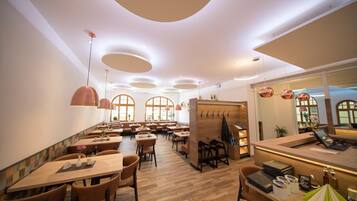 A restaurant interior with wooden tables, brown chairs, and pendant lighting.