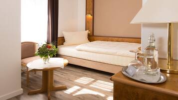 Ein Hotelzimmer mit einem Bett, einem kleinen Tisch mit Blumenvase, einem Sessel und einem Nachttisch mit Lampe und Gläsern.