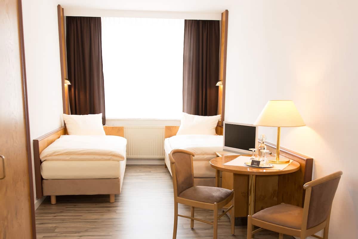 A hotel room with two beds, a desk with a lamp, and a chair.