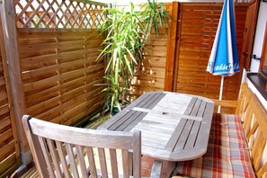 Une table et un banc en bois, installés dans un espace extérieur délimité par une clôture en bois, avec un parasol bleu.