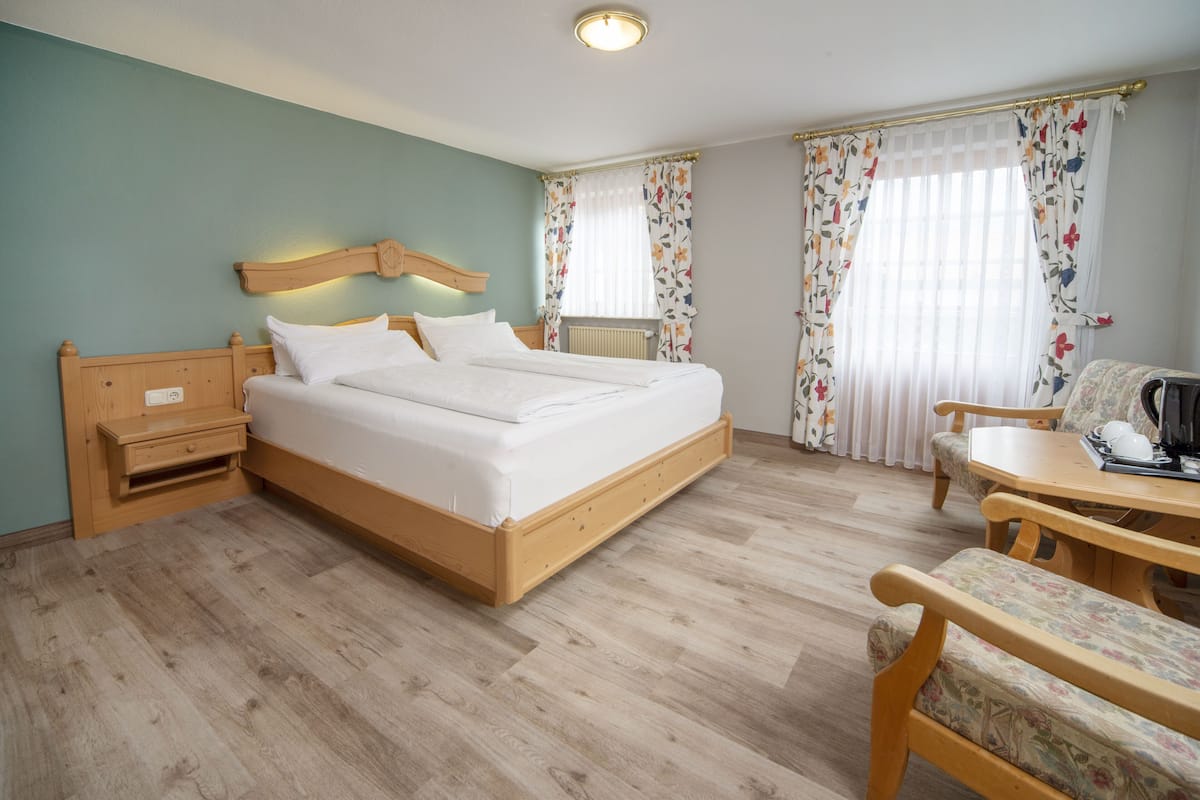Ein Schlafzimmer mit einem hölzernen Bett, einem Nachttisch, einem Stuhl und einem kleinen Tisch mit einer Lampe.