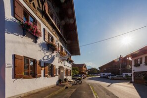 Un bâtiment traditionnel avec des volets en bois, une enseigne indiquant un restaurant, et des voitures garées le long d’une rue.