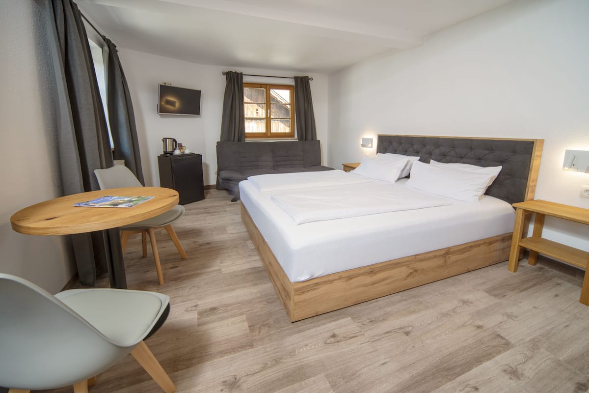 Ein Hotelzimmer mit einem großen Bett, einem kleinen Schreibtisch, einem Stuhl, einem Fernseher und einem Fenster mit Vorhängen.