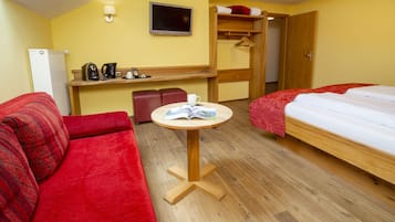 Ein Hotelzimmer mit rotem Sofa, einem Bett, einem kleinen runden Tisch mit einem Buch, einem Fernseher, einer Minibar und einem Holzschrank.