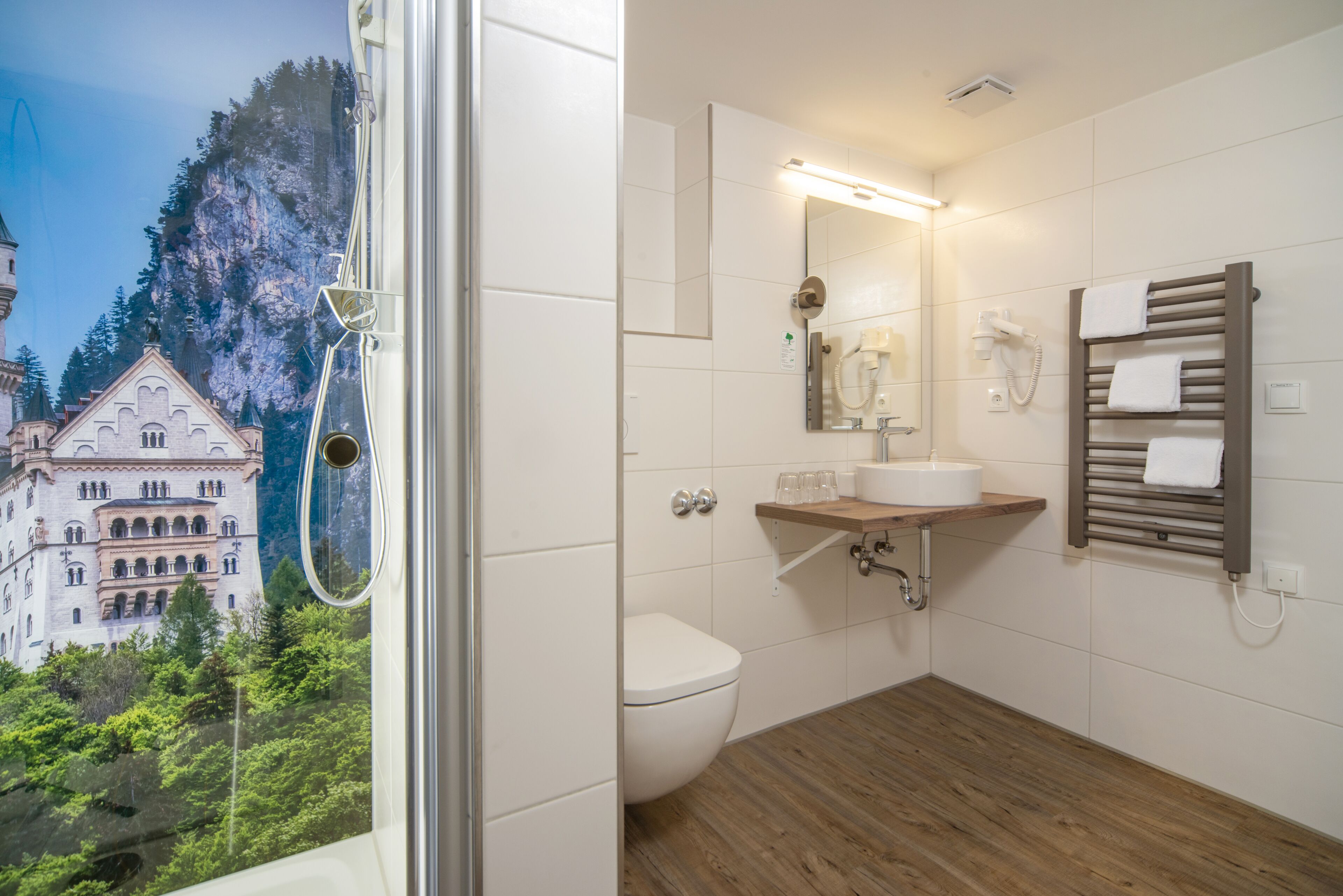 Un bagno con pavimento in legno, un WC bianco, un lavabo con specchio sopra e un porta asciugamani.