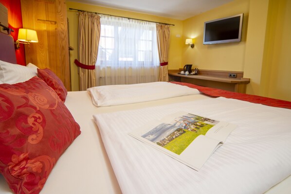 A hotel room with two beds, a TV, a desk, and a window with curtains.
