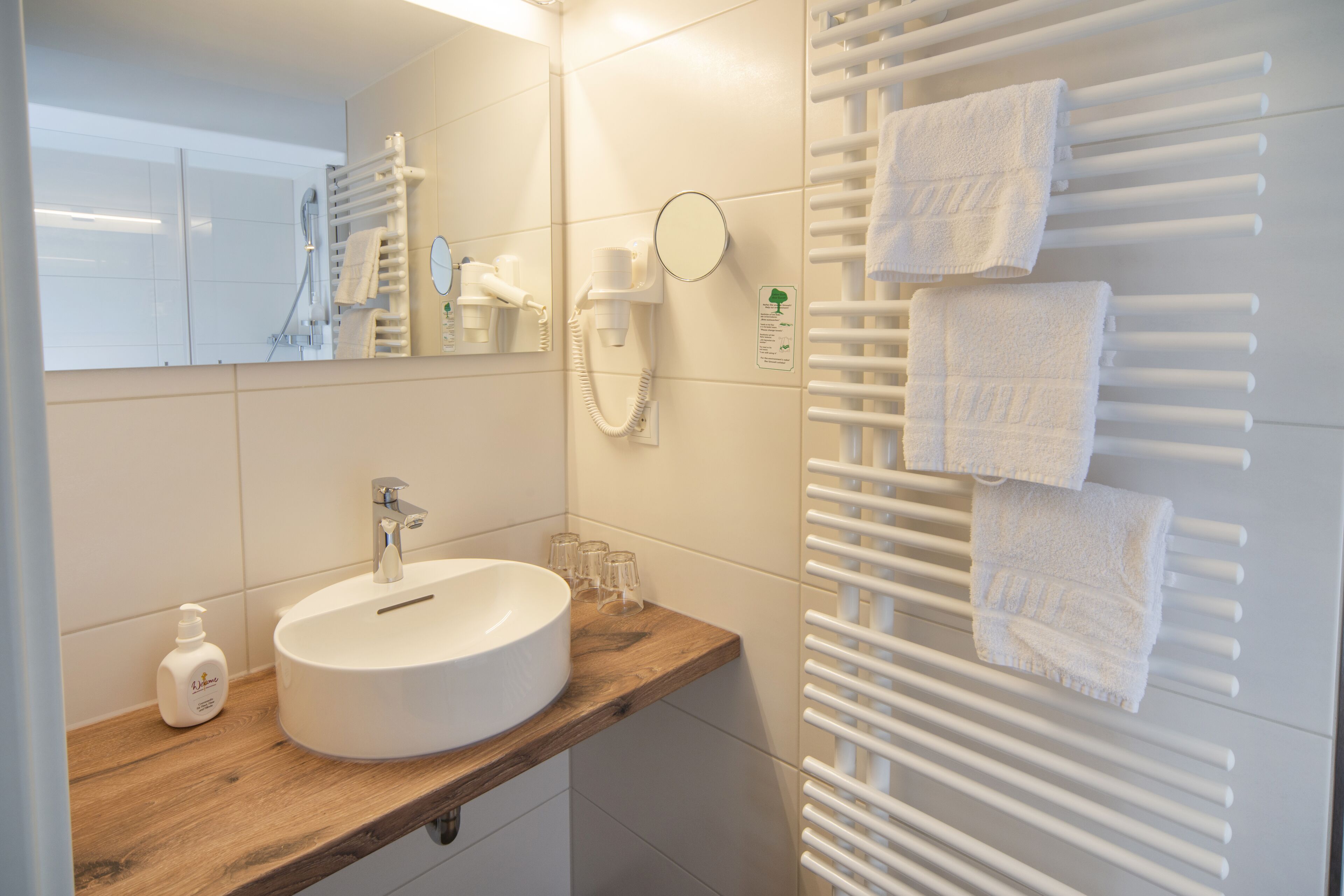 A modern bathroom with a wooden vanity, a white sink, a mirror, a towel rack, and a hand dryer.