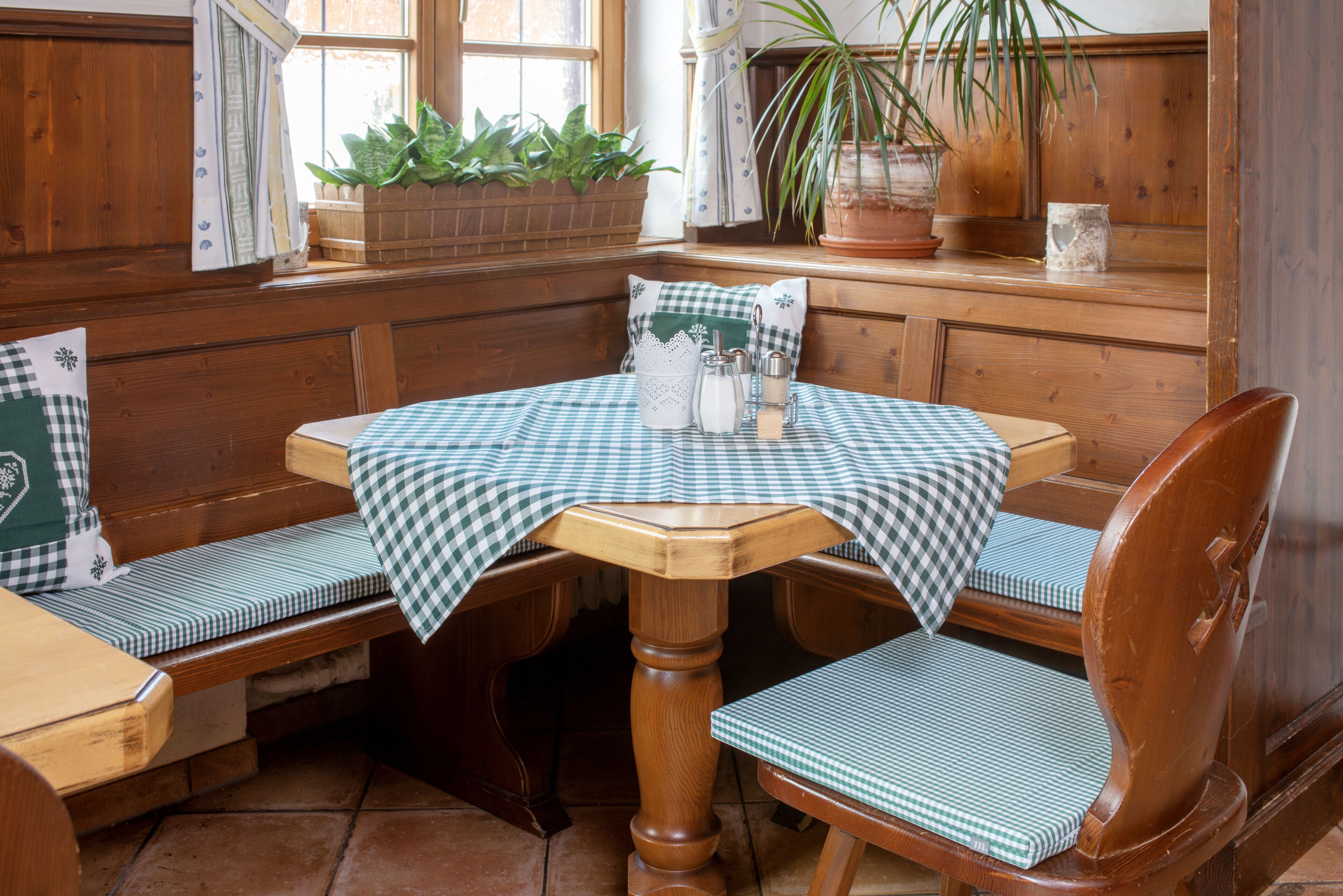 Un banco de madera con mantel a cuadros, una mesa de madera y una silla con cojín a cuadros.