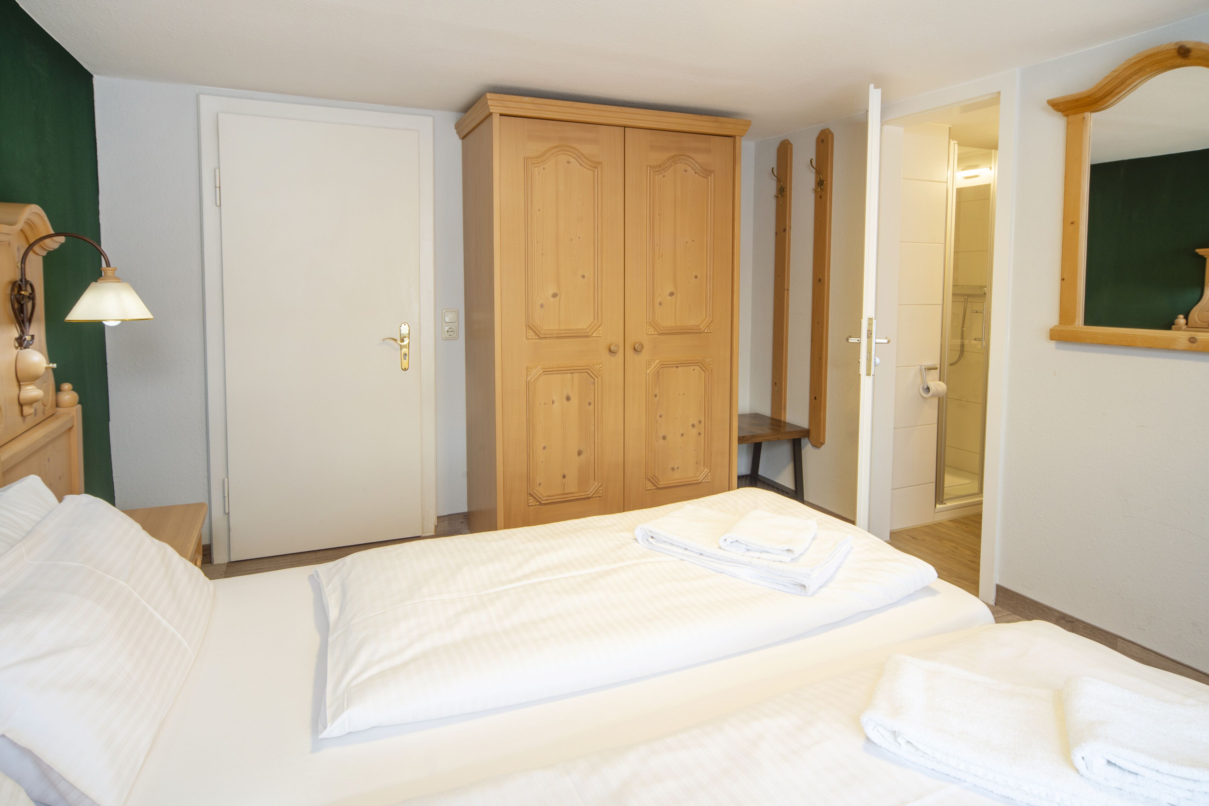 A hotel room with a bed, a wardrobe, a mirror, and a bathroom visible through an open door.