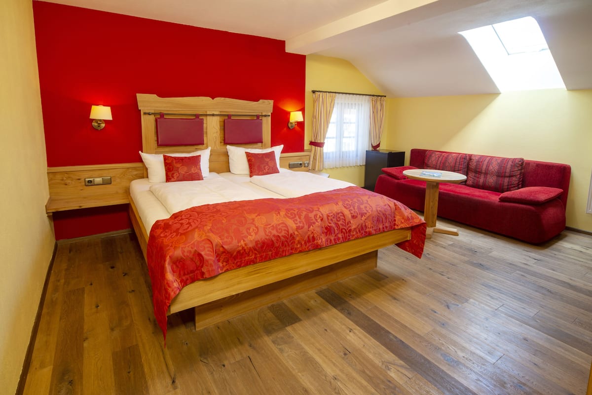 Ein Schlafzimmer mit einem großen Bett, einem roten Sofa, einem kleinen Tisch und einem Dachfenster.