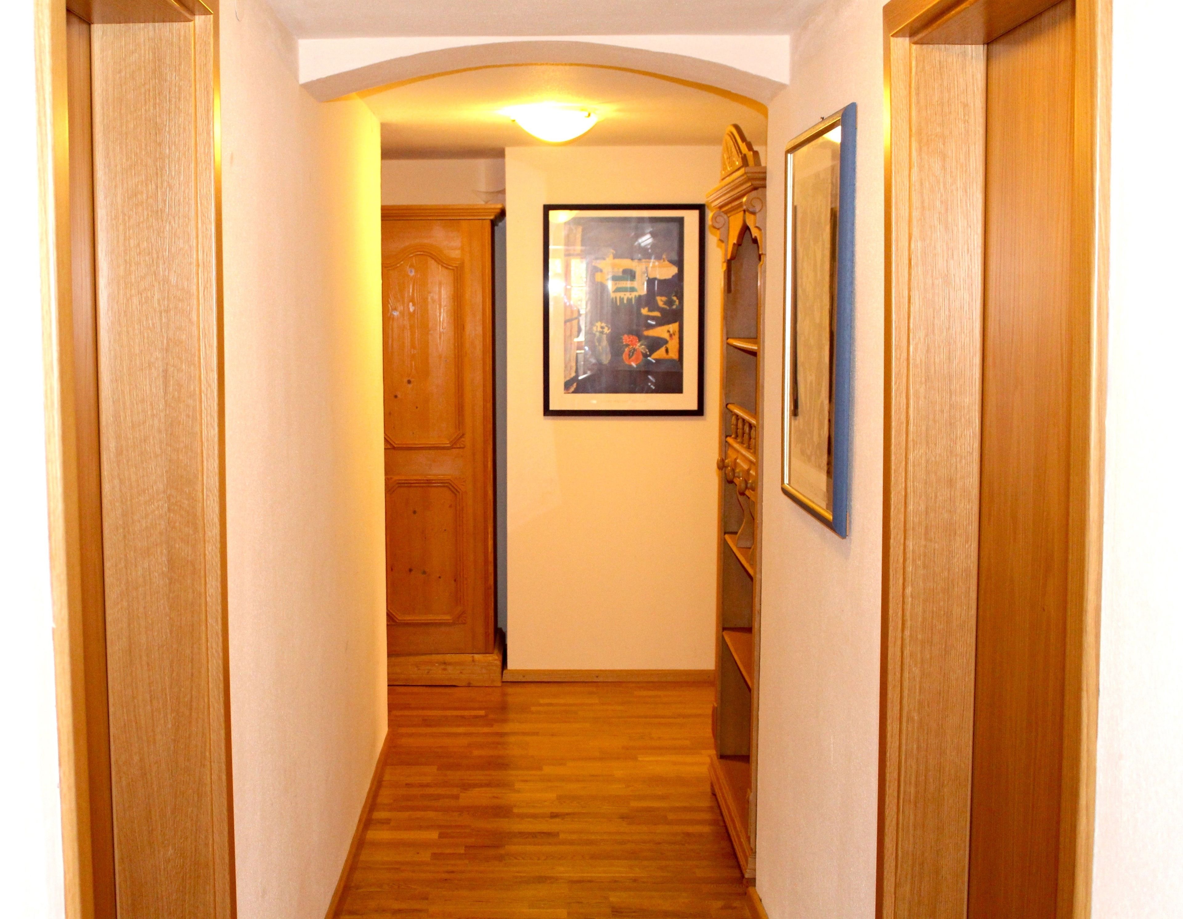 A narrow hallway with wooden doors and a framed picture on the wall.