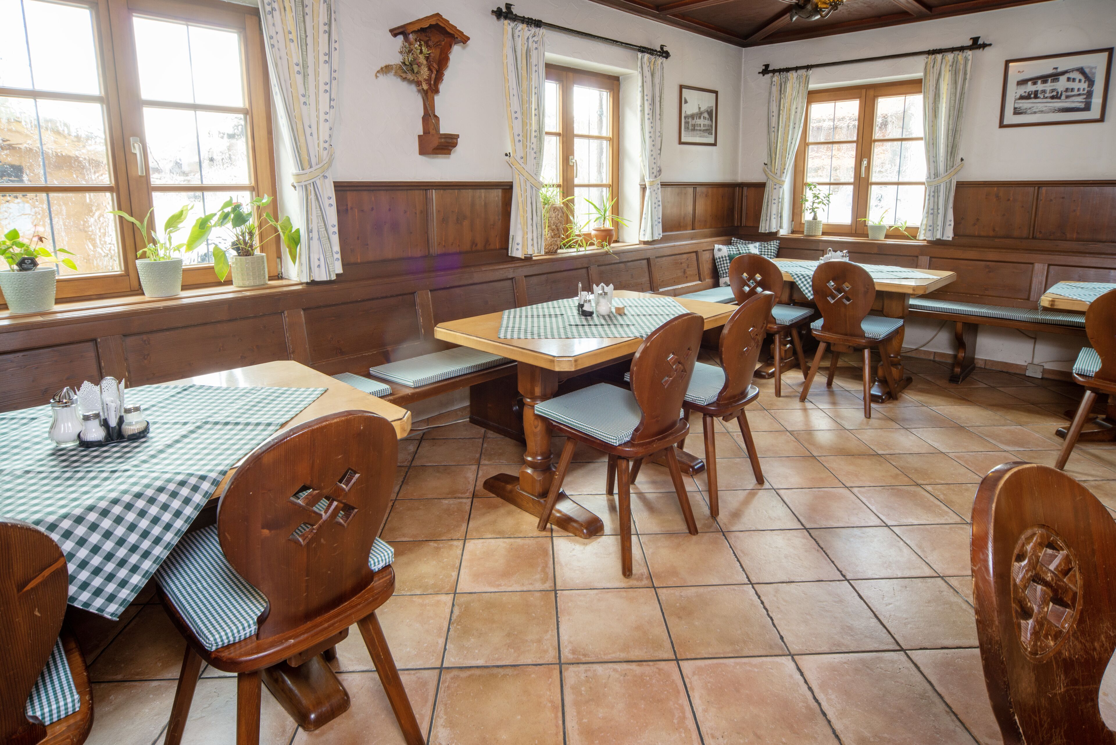 Un'osteria tradizionale con mobili in legno, tovaglie a quadretti e piante in vaso vicino alle finestre.