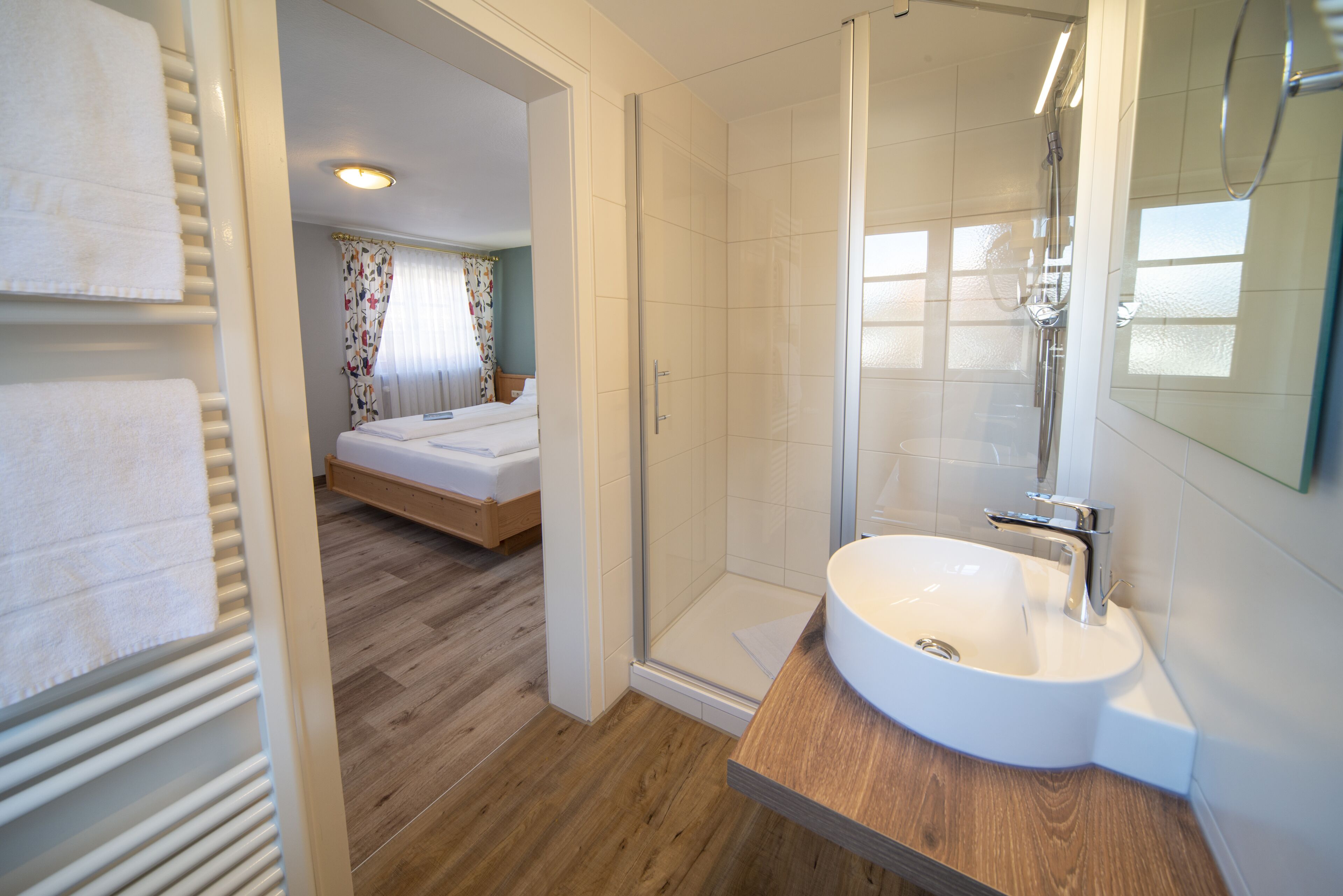 Ein modernes Badezimmer mit Duschkabine aus Glas, einem Holzanbau und einem Bett im angrenzenden Zimmer.